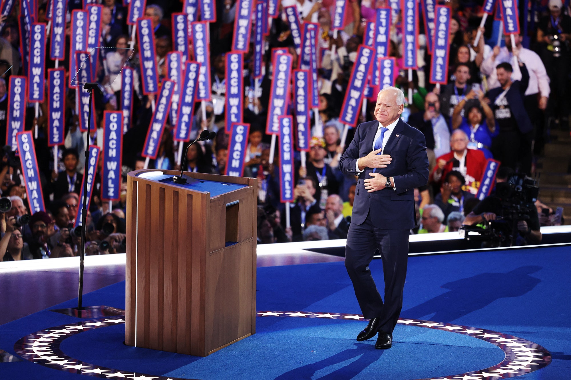 Image may contain Tim Walz Crowd Person Adult Clothing Footwear Shoe Audience Camera Electronics and Speech